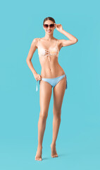 Young tanned woman in swimsuit and sunglasses on blue background