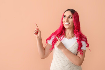 Beautiful woman with bright pink hair pointing at something on beige background