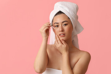 Young Asian woman with cosmetic serum on pink background