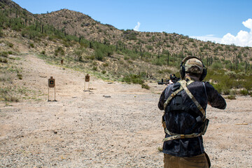 Person wearing Military vest and ear protection shooting custom ar15 pistol gun with holosight at targets down firing range