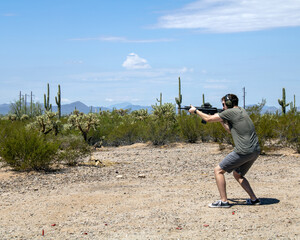 Guy shooting gun at arizona desert shooting range with cactus in background during firing drill