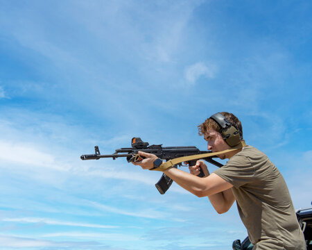 Person Holding A Modified Ak47 Assault Rifle With Strap While Shooting Targets And Wearing Ear Protection With A Blue Sky In Background For Silhouette