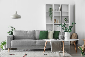 Interior of light living room with grey sofa, table and shelving unit