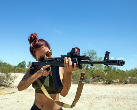 Cute girl wearing crop top holding a custom Russian AK-47 assault rifle with holosight in Arizona Desert