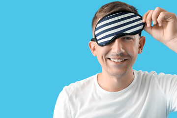 Young man with sleeping mask on blue background