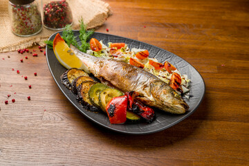 Fried sea bass with grilled vegetables on black plate