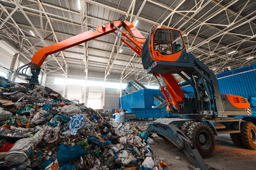 Excavator grabs trash in warehouse of waste processing plant
