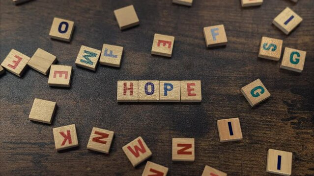 Top view of a dark-wood table and scattered wooden square letter puzzles creating the word HOPE. Symbolic. High quality 4k footage