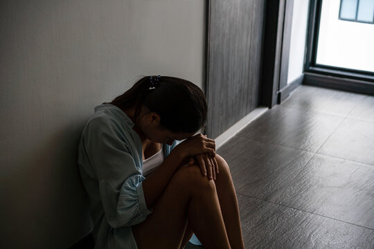 Stressed young Asian woman suffering on depression and sitting alone outside the room or hallway of apartment. Sad, unhappy, disappointed, domestic abuse or stop violence and rape concept. Copy space