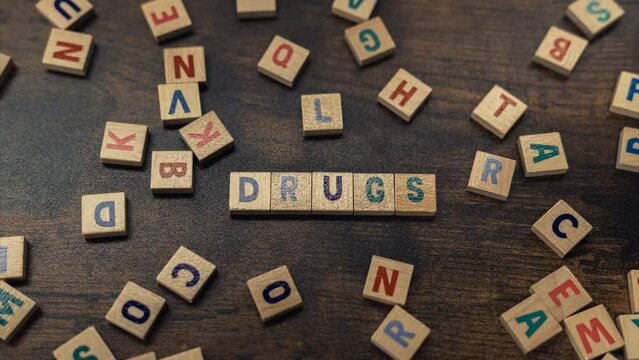 The dangerous concept of drug abuse depicted by symbolic word puzzles creating the word DRUGS from square wooden letters in the shades of blue. High quality 4k footage