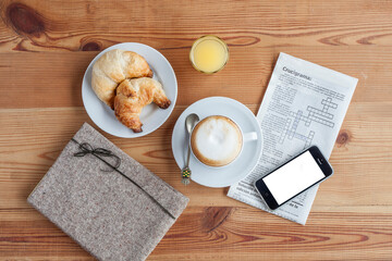 Breakfast with coffee, croissant, orange juice, a cell phone and a crossword puzzle