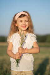 Portrait of a beautiful little girl with blonde hair. The child walks in the field and collects a bouquet. Model appearance in a child