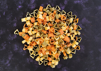 Colorful dry love pasta on dark background. Top view