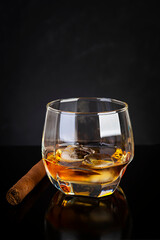 Glass of whiskey and cigar on dark background.