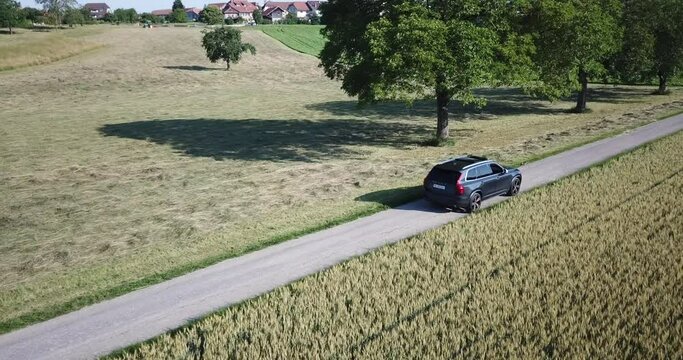 A Volvo car drives on a small road near a village in the swiss countryside, Vaud, drone shot