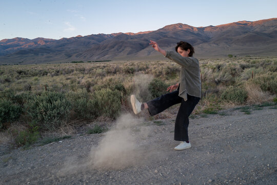Bored hiker kicks up dust on side of gravel road in empty rural landscape