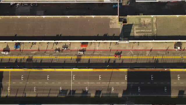 Aerial tracking shot of racing cars driving into pit stop during race on Autodromo at sunset