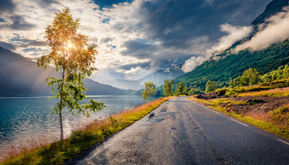 Fototapeta premium Dramatic summer view of Lovatnet lake with asphalt road. Foggy morning scene of Sogn og Fjordane county, Norway, Europe. Traveling concept background..