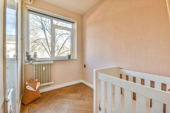 Interior of white room with baby crib and armchair near window with blue chest of drawers in daylight