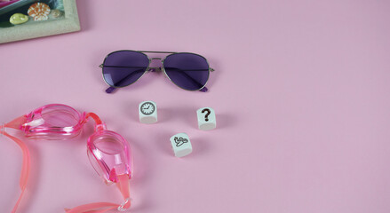 Pink background sunglasses, with picture frame, goggles , cubes with airplane, clock and question mark. A beautiful layout on the theme of planning a family vacation. 