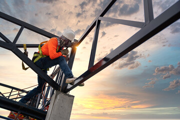 A Steel roof truss welders are working on the roof structure with safety devices to prevent fall...