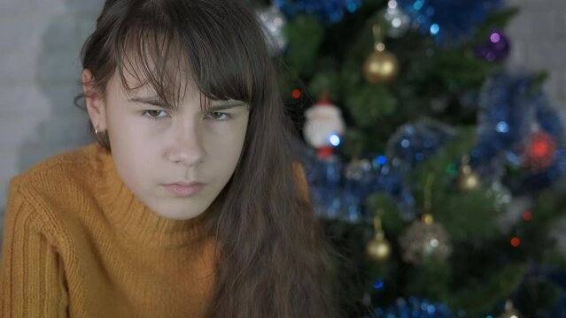 Displeasure at Christmas. A teen girl with displeasure stay in the decorated Christmas room.