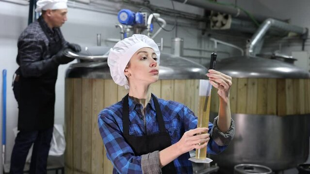 Focused skilled young female brewery worker using digital hydrometer for measuring craft beer density. High quality FullHD footage