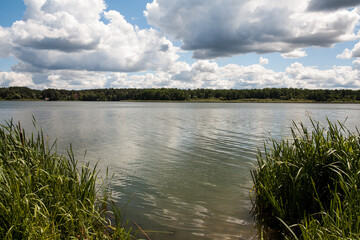 Picturesque landscape with a cloudy sky and a wide river. In the distance, across the river, there is a forest. An image as a background for your travel and nature illustrations.