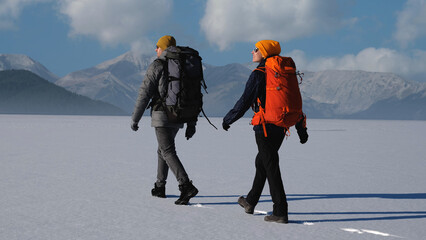 The man and woman with backpacks walking on a snowy mountains background