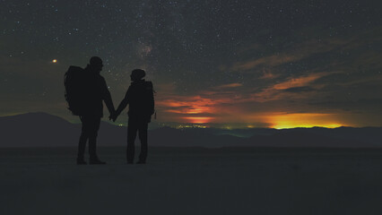 The man and woman with backpacks standing on a starry sky background