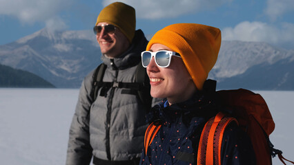 The two travelers with backpacks standing on a snowy mountains background