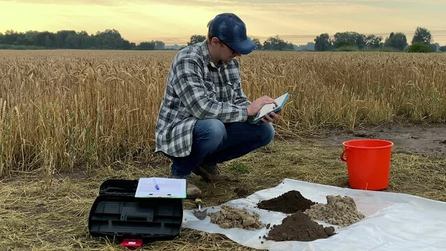 Agricultural scientist using tablet, entering data looking at sampling information sheet during soil testing at dawn outdoors. Farmer using digital device at field. Environment research, certification