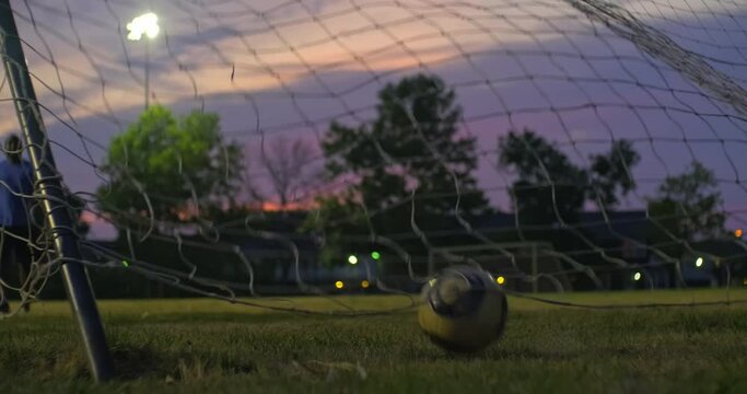 Behind the goal net view of a soccer - football player practicing a penalty kick under the flood lights on a beautiful summer evening