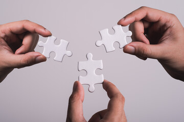 three hands trying to connect couple puzzle piece with gray background. Jigsaw puzzle team work concept. one part of whole. symbol of association and connection. business strategy. - obrazy, fototapety, plakaty