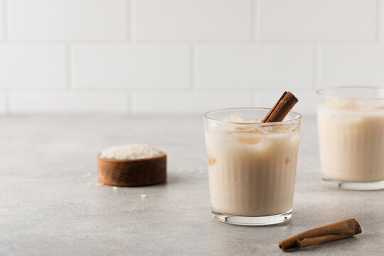 Homemade Horchata rice drink in a glass with ice and cinnamon stick on a gray concrete background. Copy space.