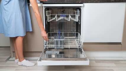A woman's hand extends or pushes the bottom shelf of an empty dishwasher