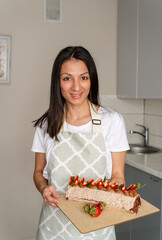 Woman decorated with berries a biscuit cake with white cream. Cake stands on a table. Homemade pastry, cooking cakes. Housewife female chef cook confectioner or baker in apron white t-shirt.