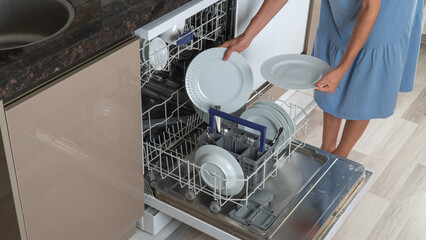 A woman folds clean dishes from a dishwasher