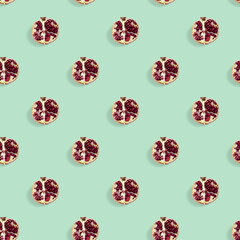 Seamless pattern made of ripe pomegranate fruit cut in half on green background