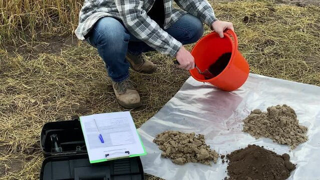 Male agronomist taking soil sample out from bucket with garden trowel on plastic underlay outdoors. Heaps of different soil types arranged on test area. Environment research, soil certification