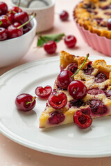 Slice of clafoutis with cherry on white plate. Traditional homemade french cherry pie. Selective focus.