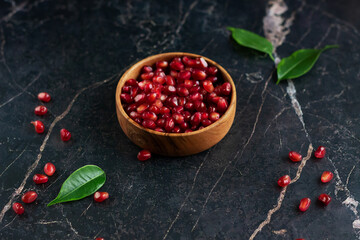 Pomegranate seeds in wood bowl with seeds on black marble table