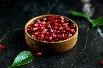 Pomegranate seeds in wood bowl with seeds and leaves on black marble table