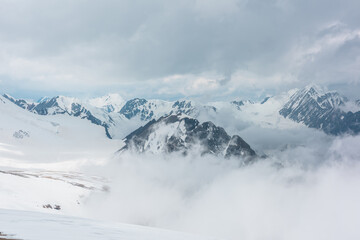 Awesome aerial view to high snowy mountains in dense low clouds. Minimal landscape with beautiful mountain peaks in thick clouds. Simple minimalism with snow mountain tops in cloudy sky above clouds.