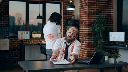 Creepy mindless zombie sitting in office while working on modern laptop. Spooky brain dead monster...