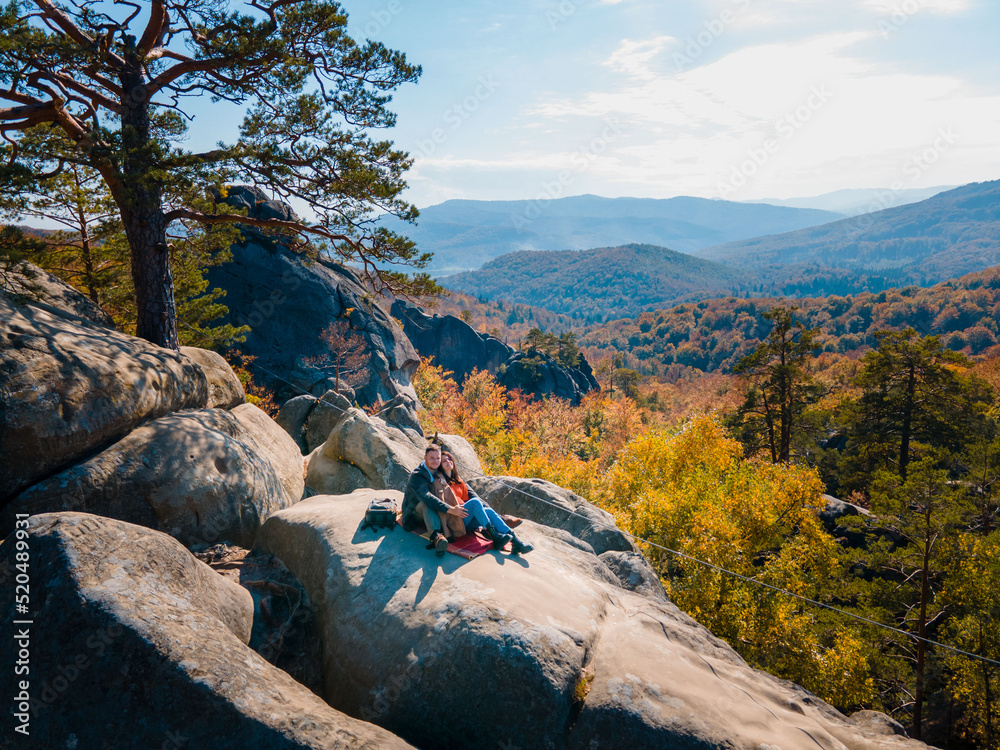 Wall mural couple traveler sitting on the top of the rock with beautiful landscape of autumn forest