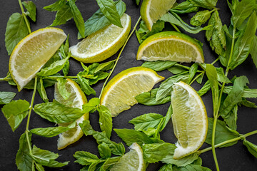 Lime slices and mint sprigs on a black background. Lime and mint. Summer freshness. Natural background. Ingredients of lemonade. Yellow and green colors in still life. A sprig of mint. Sliced lime.