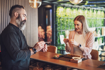 Sushi master is teaching young woman how to use chopsticks at sushi restaurant.