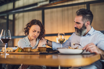 Adult couple is sitting at restaurant. They are having dinner with wine. Woman is sad and depressed.