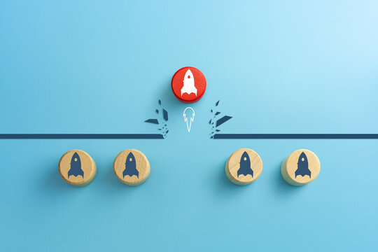 Concept of overcoming barriers, goal, target. Red wooden cube with rocket launch icon breaking through obstacle on blue background